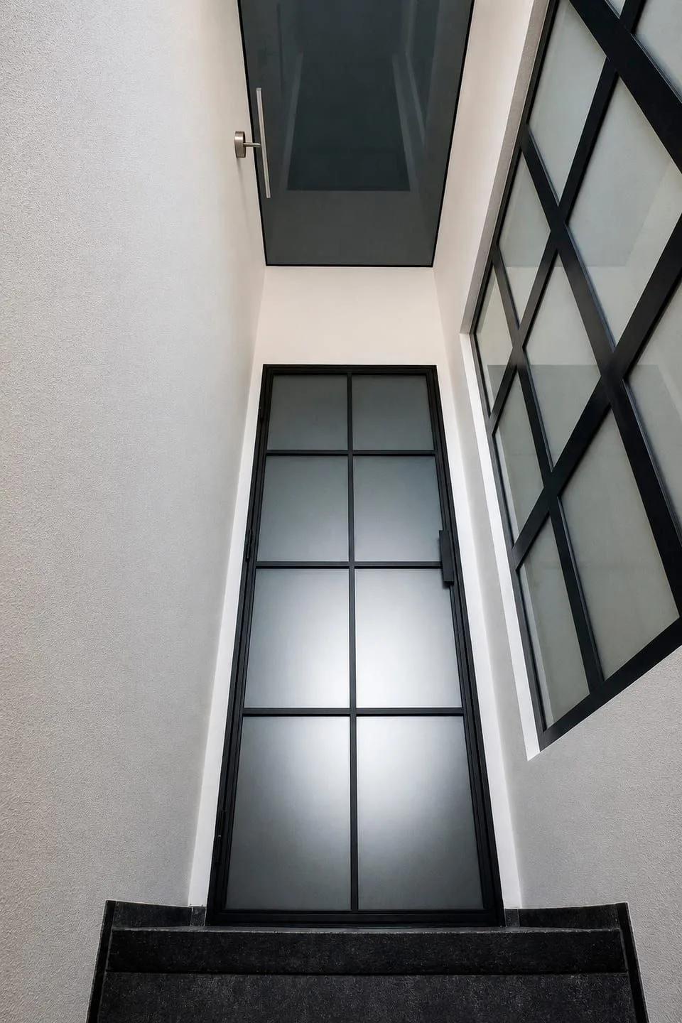 Černě rámované okno u schodiště rodinného domu